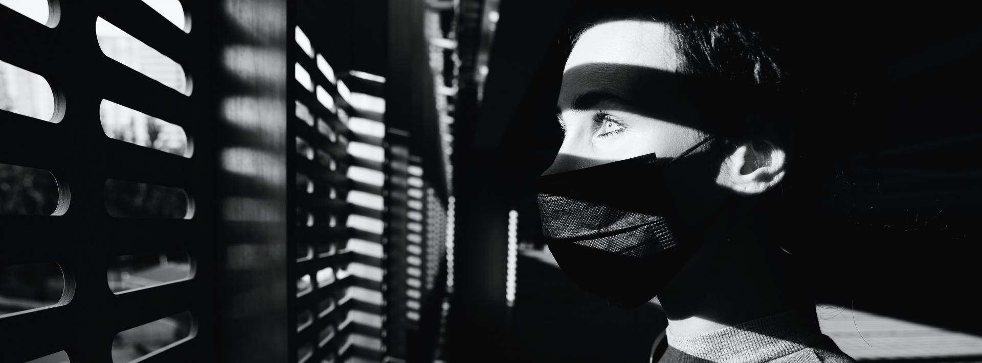 woman wearing mask while looking out blinds - black and white image