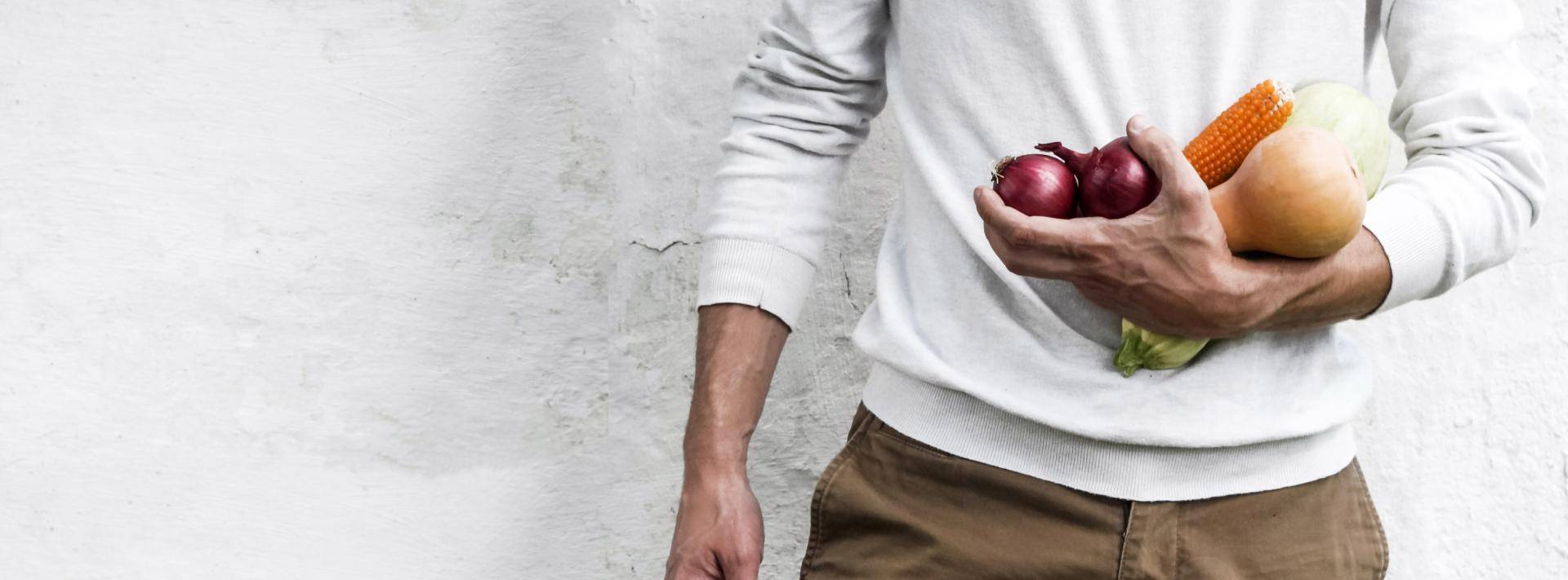 Man standing against white wall holding vegetables