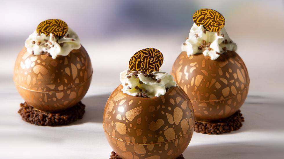 Dessert shells filled with iced coffee and whipped cream, with a chocolate plaque on top