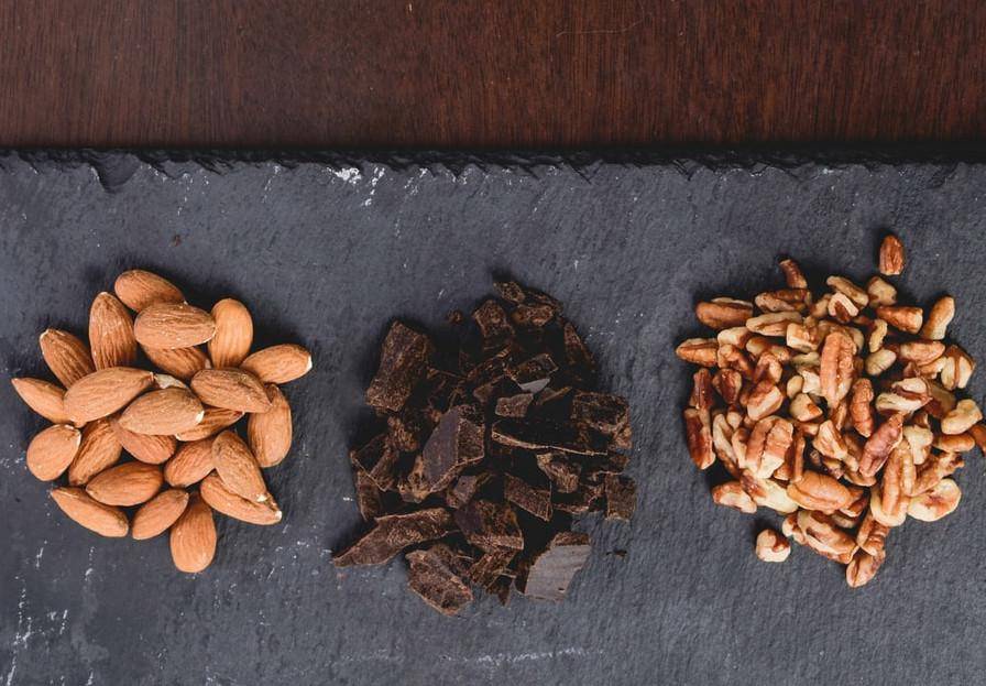 black cutting board with almonds, chocolate, and pecans