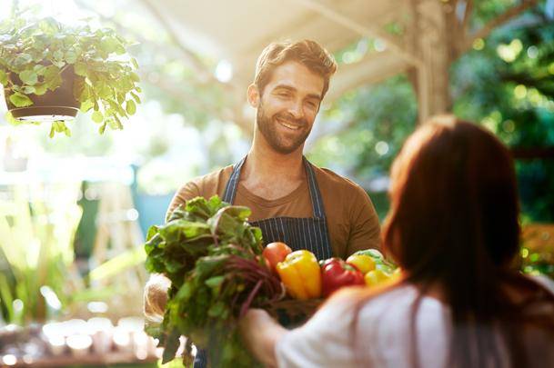 man offering vegetables to someone at a farmer's market