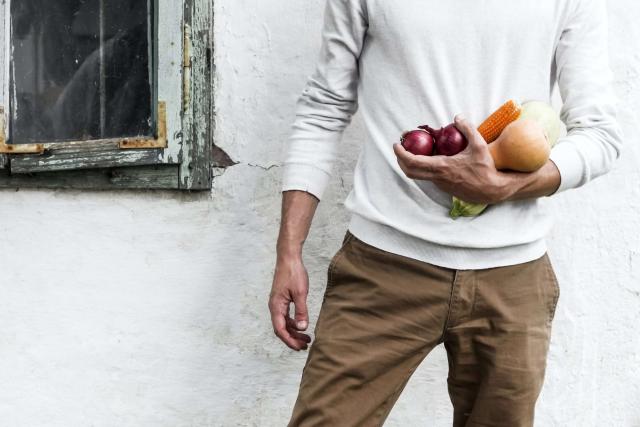 Man standing against white wall holding vegetables